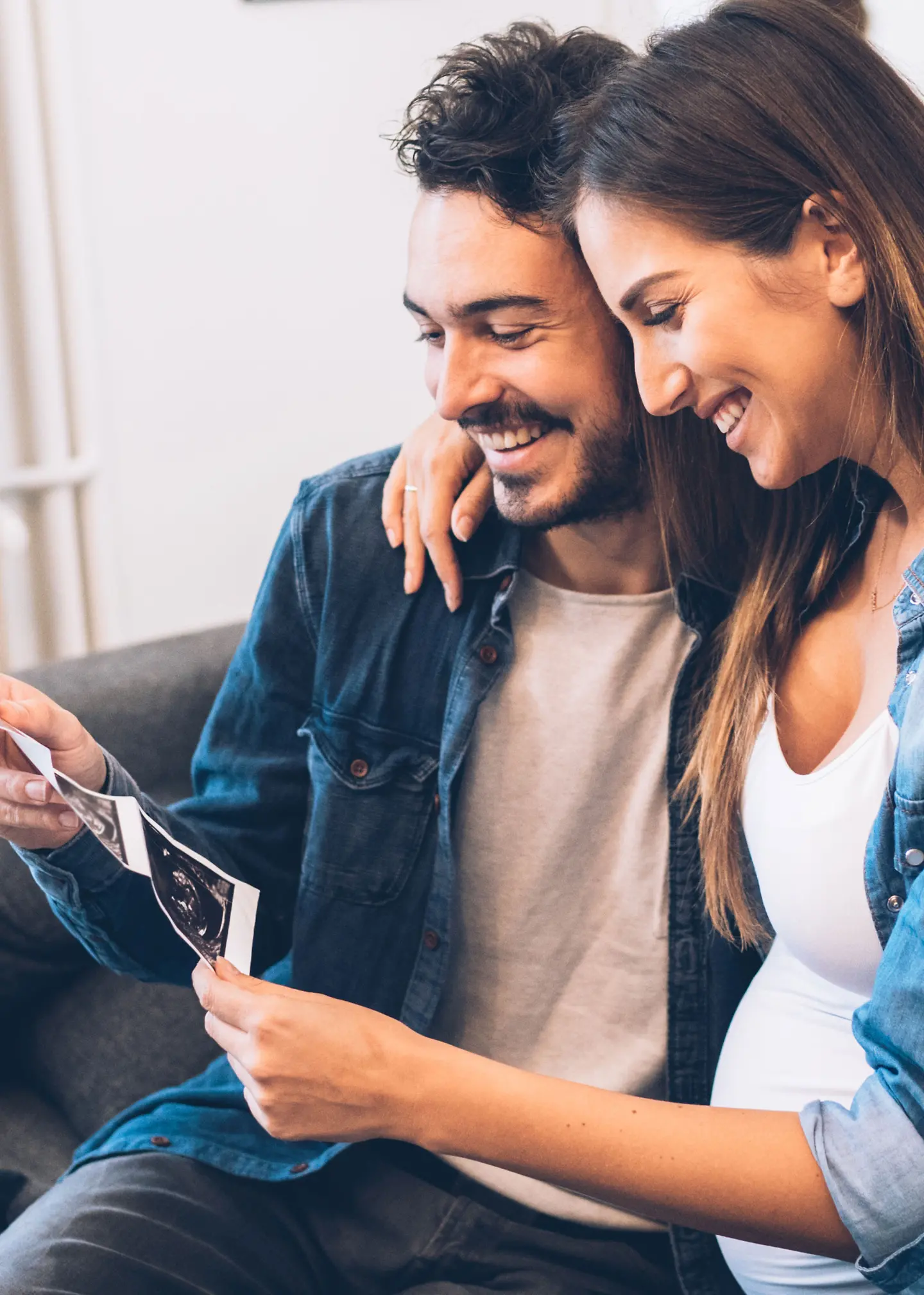 Ein Mann und eine schwangere Frau schauen sich auf einer Couch ein Ultraschallbild an