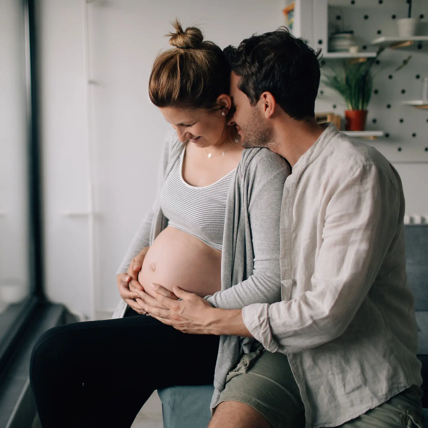 Ein Mann legt seine Kinn auf die Schultern einer schwangere Frau und beide halten den Babybauch