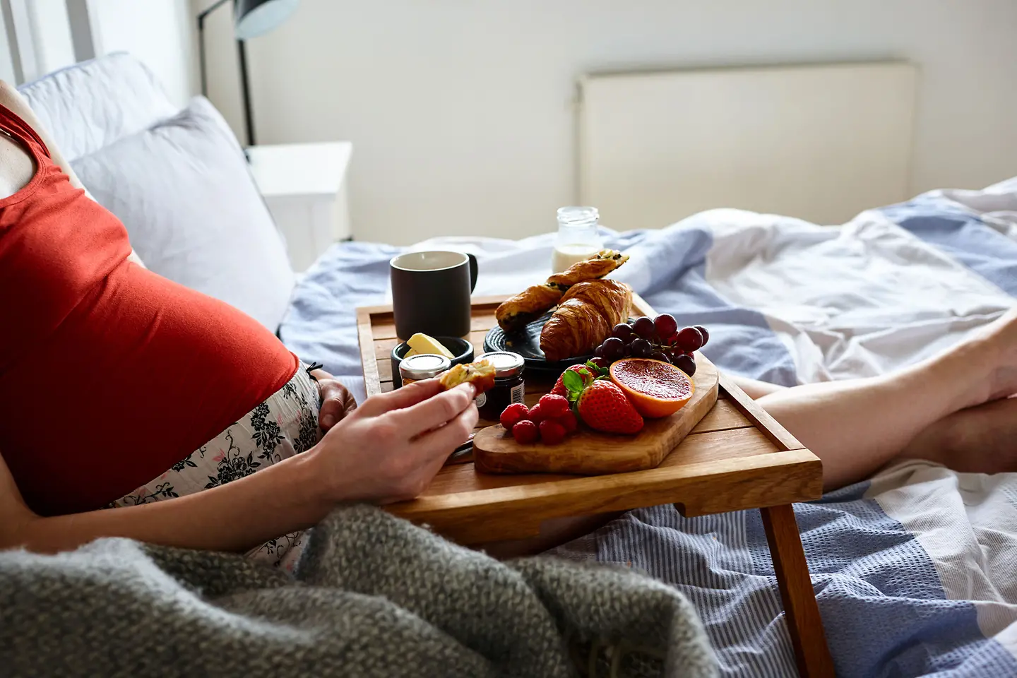 Schwangere Frau in der etwa 22. Schwangerschaftswoche liegt im Bett und Isst Frühstück auf einem Tablett