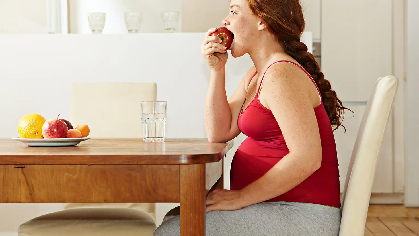 Schwangere Frau in der etwa 23. Schwangerschaftswoche beißt in einen Apfel