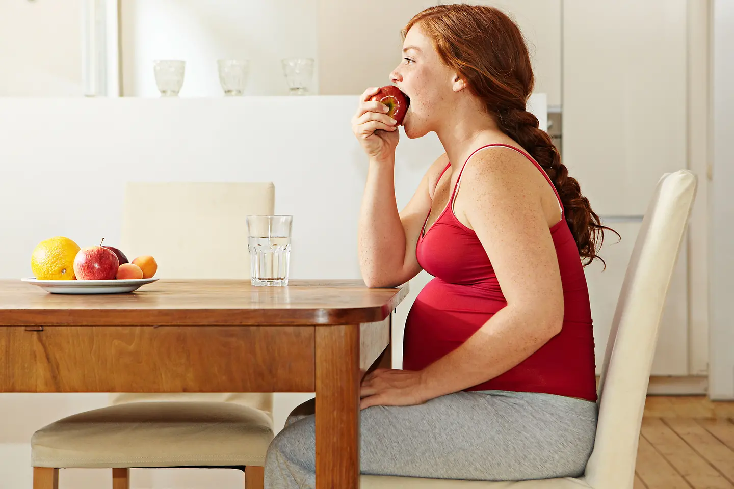 Schwangere Frau in der etwa 23. Schwangerschaftswoche beißt in einen Apfel