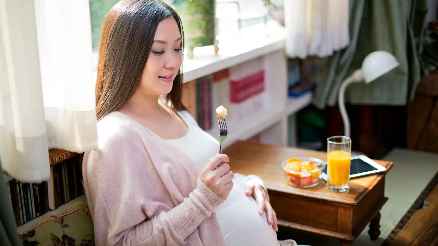 Schwangere Frau in der etwa 24. Schwangerschaftswoche hält Gabel mit Käse in der Hand
