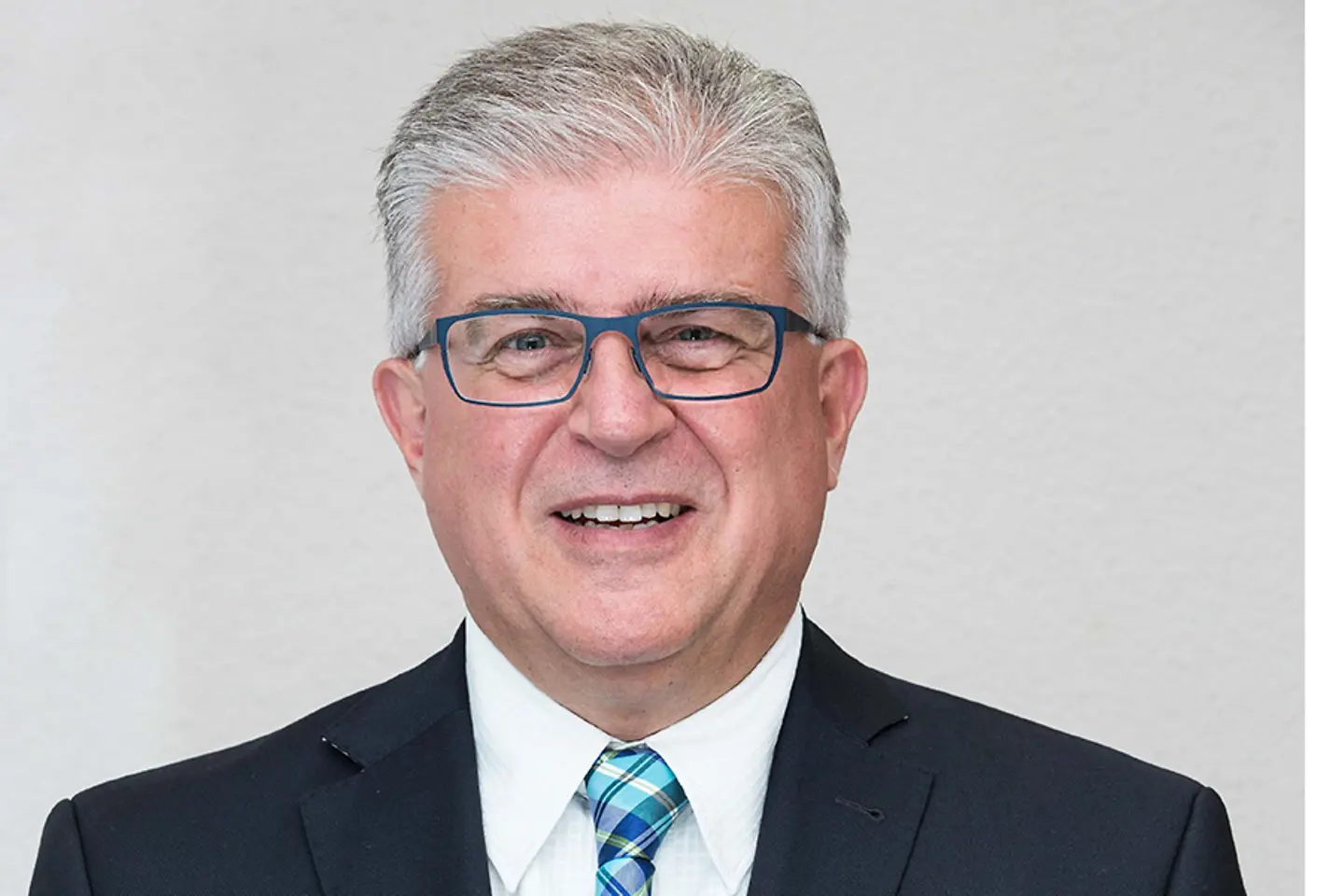 Ein Mann mit Brille, grauen Haaren und Anzug lächelt in die Kamera