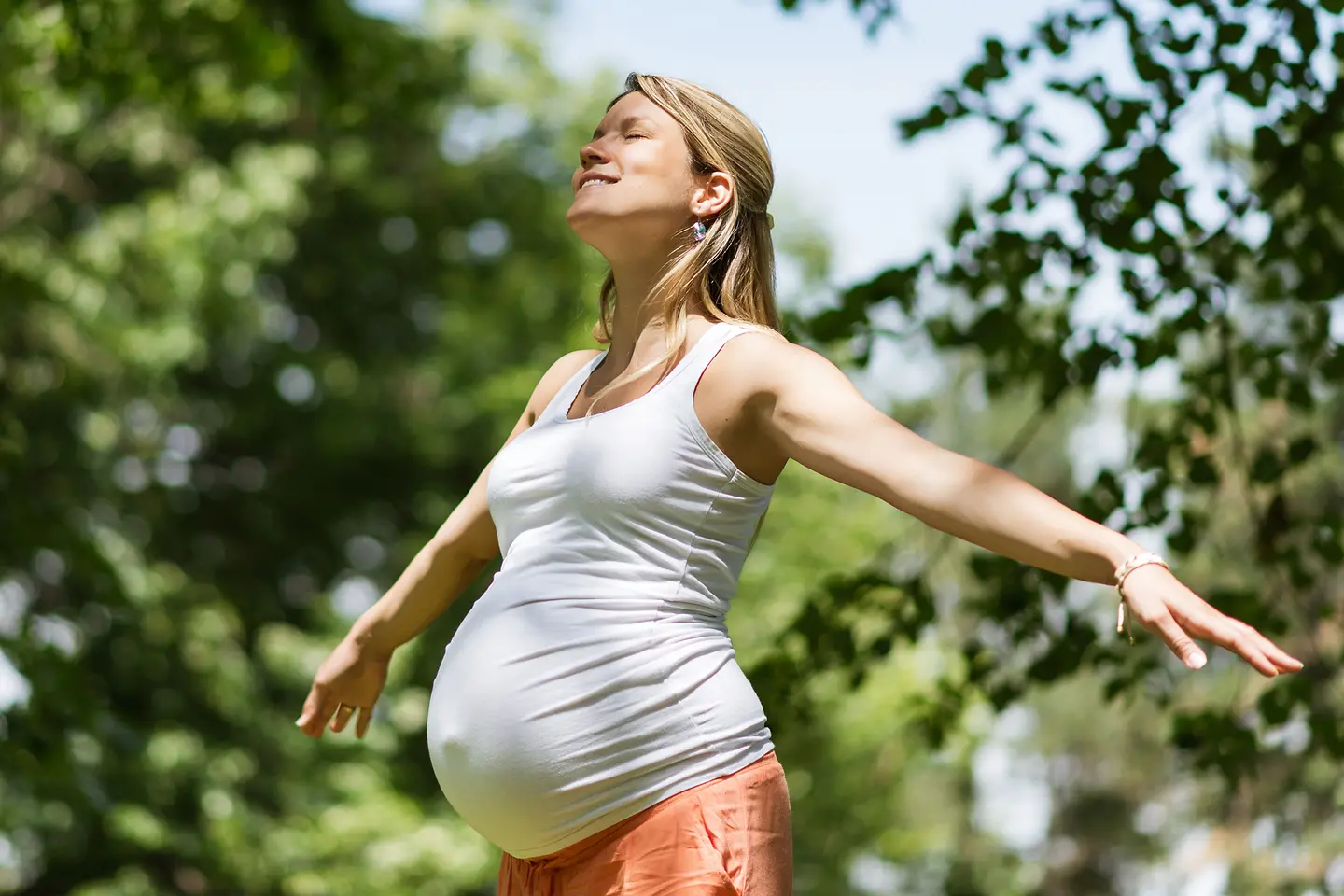 Schwangere Frau in der etwa 27. Schwangerschaftswoche genießt die Sonne mit geschlossen Augen