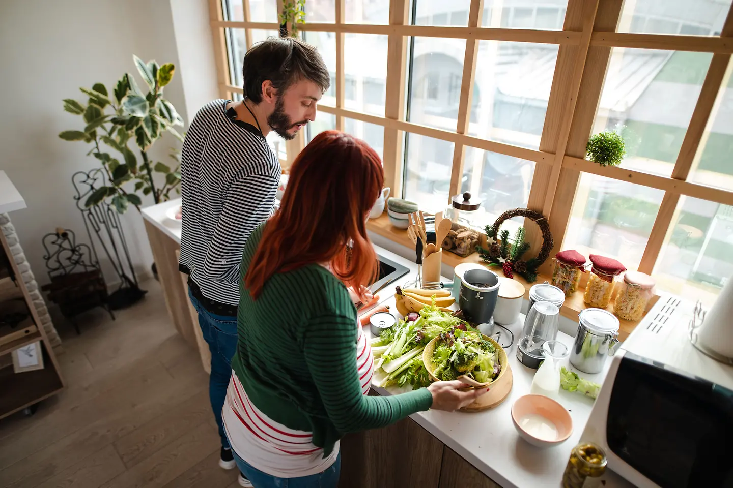Schwangere Frau um die 29. Schwangerschaftswoche und Mann stehen in der Küche an der Arbeitsplatte und bereiten einen Salat zu