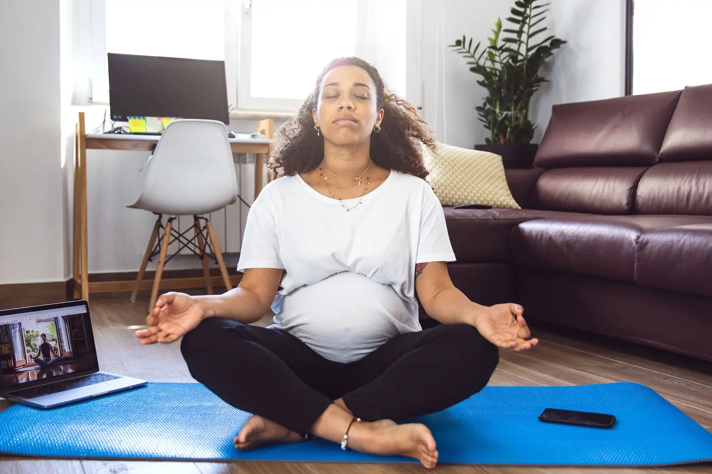 Schwangere Frau in der etwa 28. Schwangerschaftswoche meditiert im Schneidersitz auf einer Jogamatte