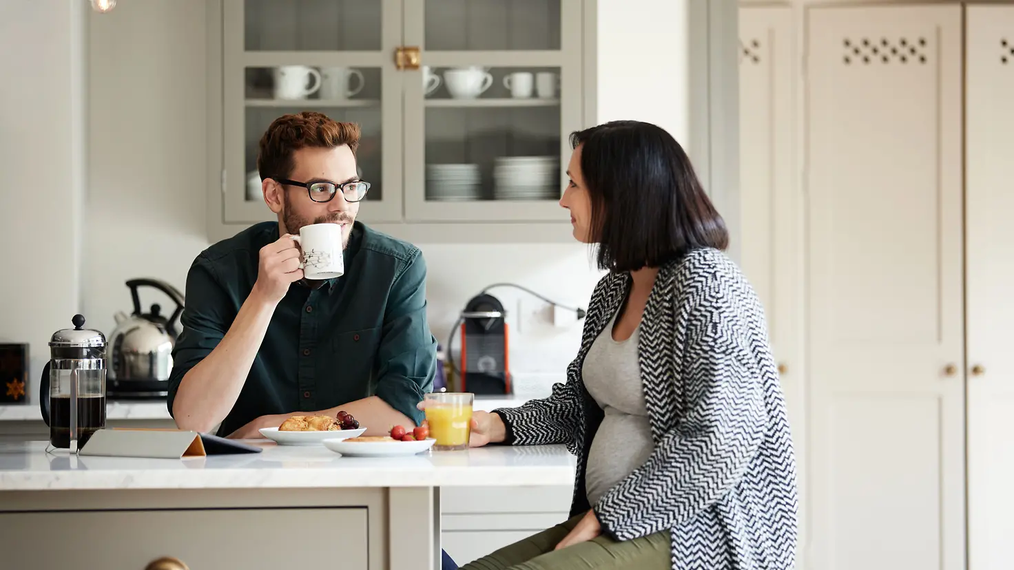 Mann und schwangere Frau um die 34. Schwangerschaftswoche sitzen beim Frühstück in der Küche