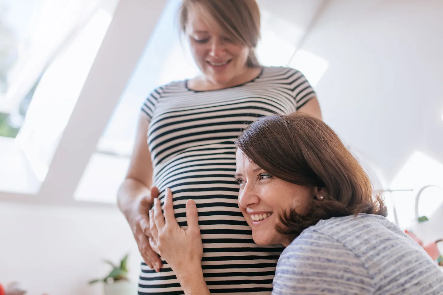 Frau horcht am Bauch einer Schwangeren um die 35. Schwangerschaftswoche