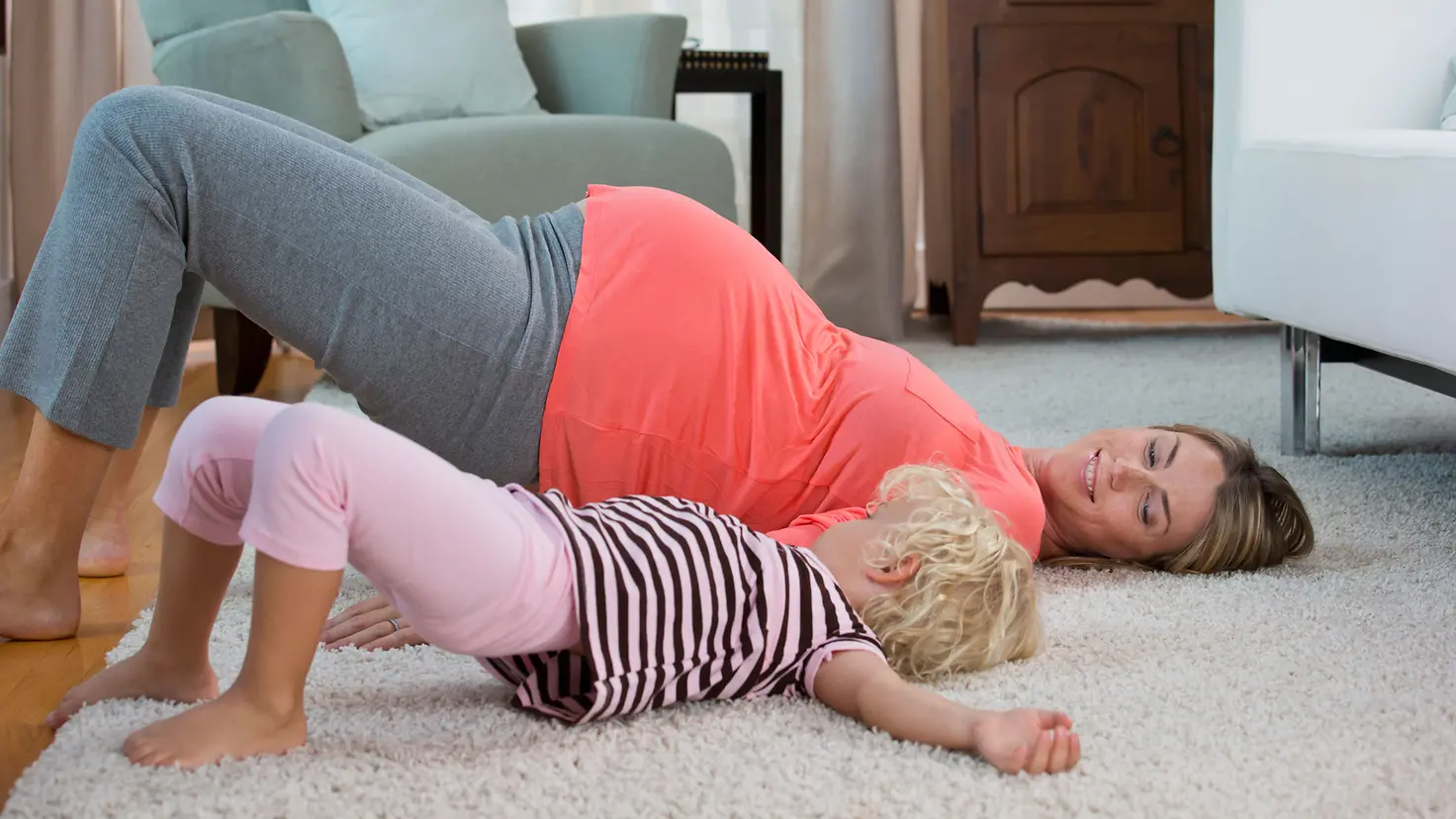 Schwangere Mutter um die 32. Schwangerschaftswoche und Tochter praktizieren Yoga auf dem Teppich