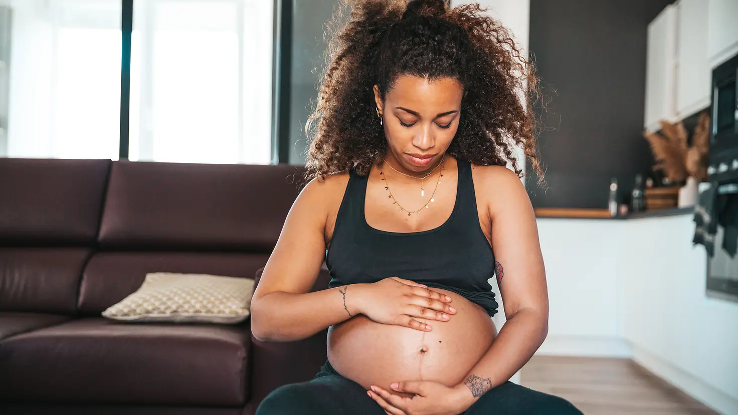 Frau um die 35. Schwangerschaftswoche sitzt und hält sich den Babybauch