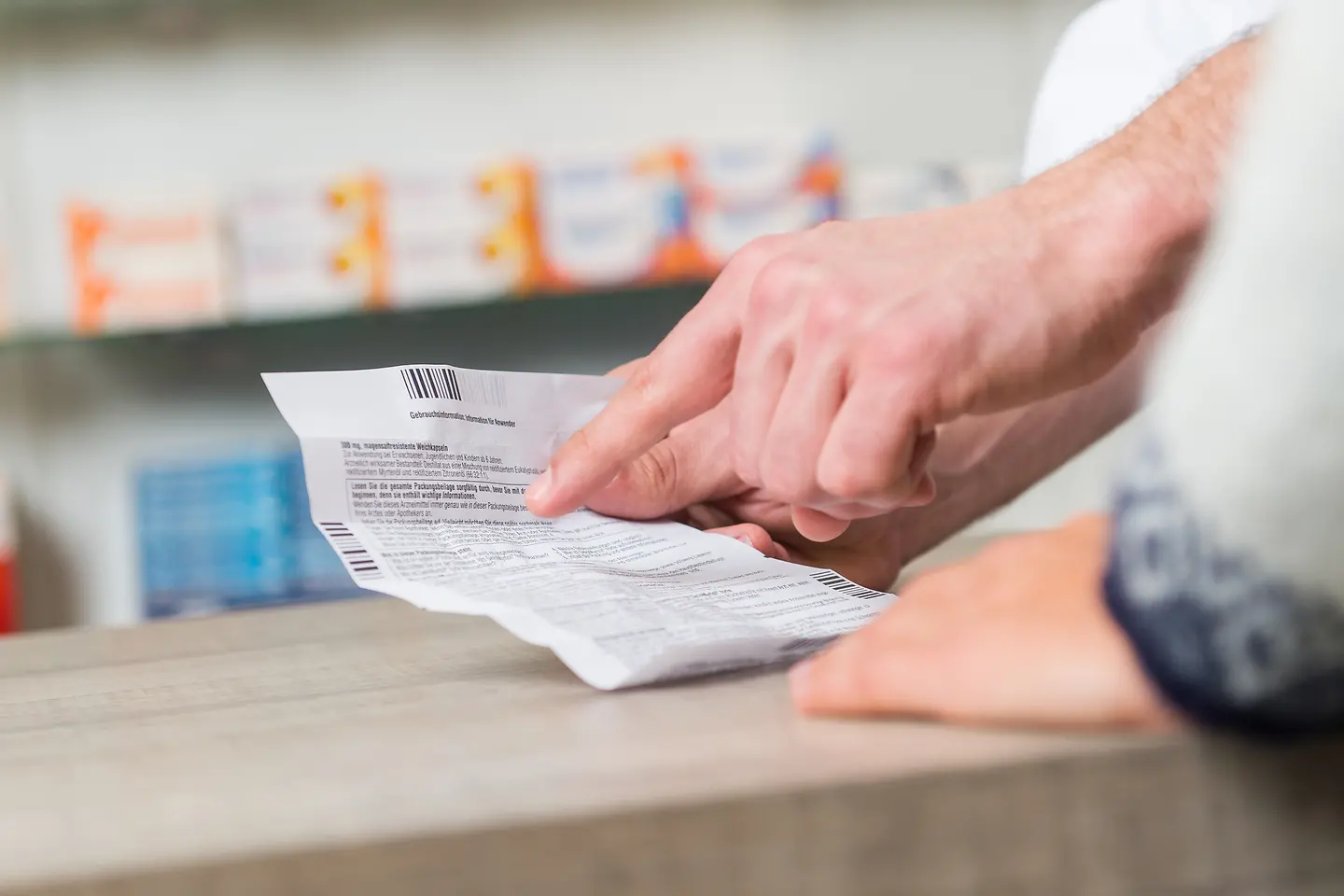 Das Bild zeigt die Hand einer Person in einer Apotheke mit einem Beipackzettel.