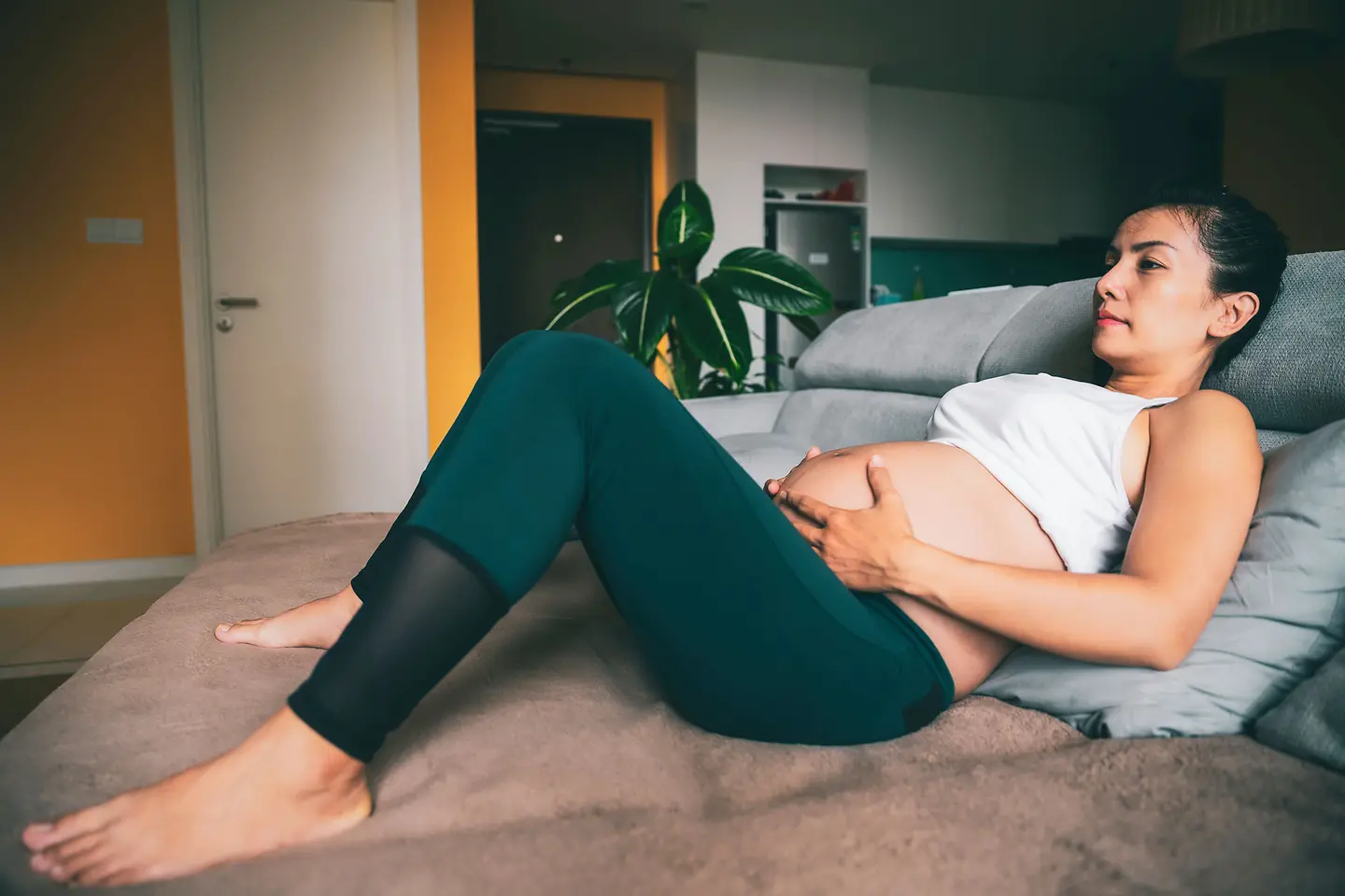 Eine schwangere Frau um die 37. Schwangerschaftswoche liegt auf einem Bett und hält sich den unteren Babybauch