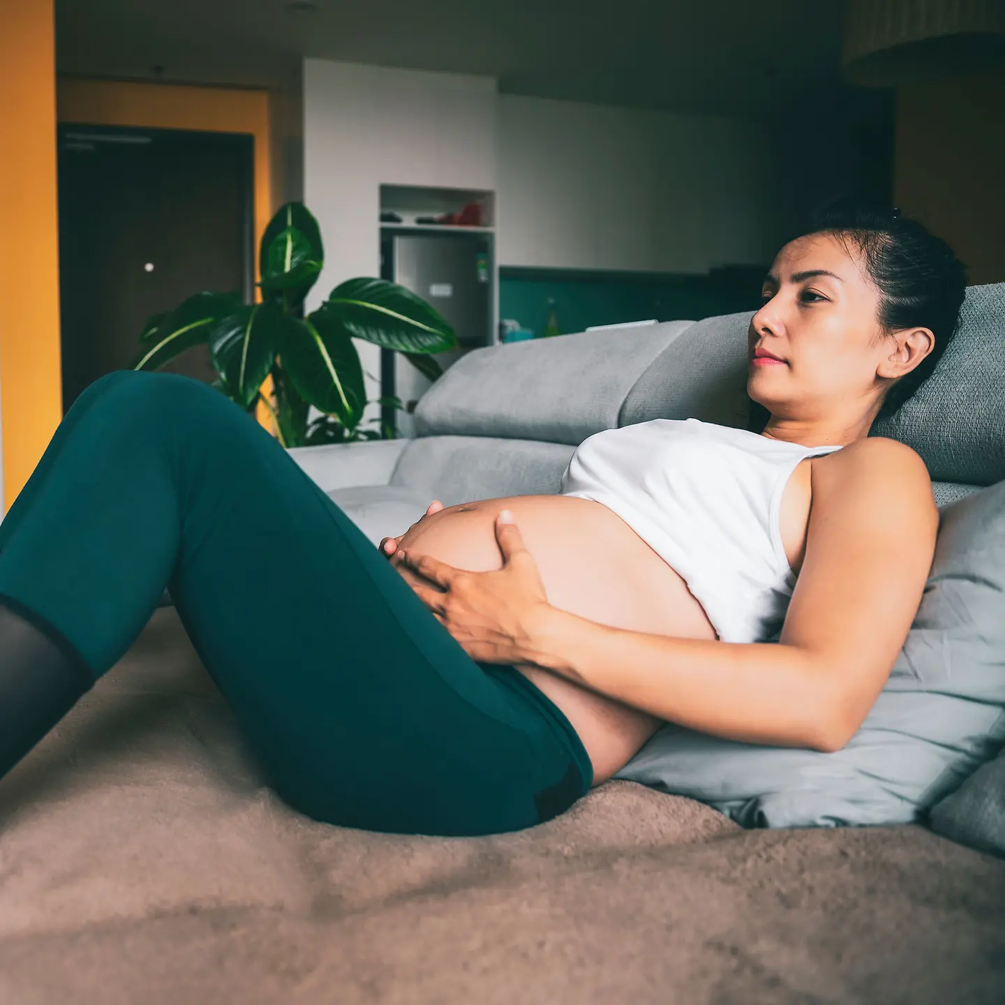 Eine schwangere Frau um die 37. Schwangerschaftswoche liegt auf einem Bett und hält sich den unteren Babybauch