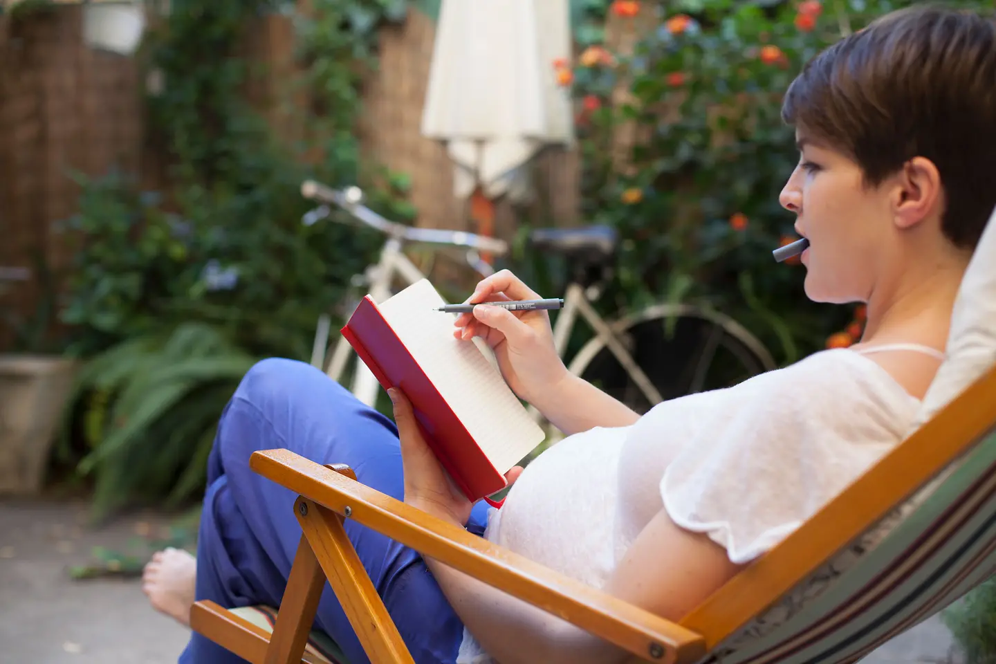 Schwangere Frau um die 38. Schwangerschaftswoche, die sich draußen auf dem Liegestuhl entspannt und Notizen macht