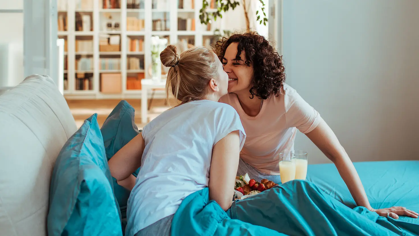 Zwei junge Frauen küssen sich über einem Frühstück im Bett