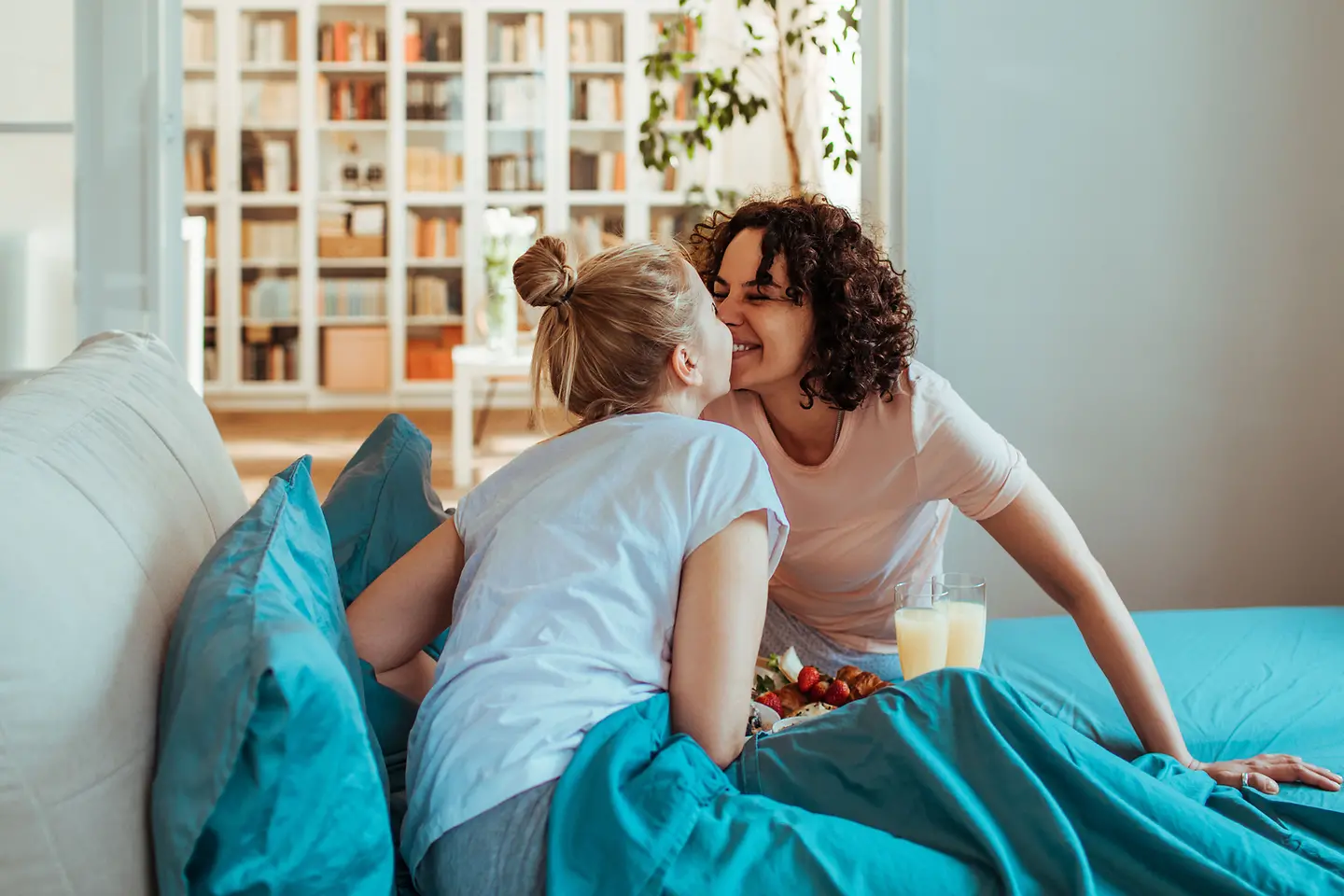 Zwei junge Frauen küssen sich über einem Frühstück im Bett
