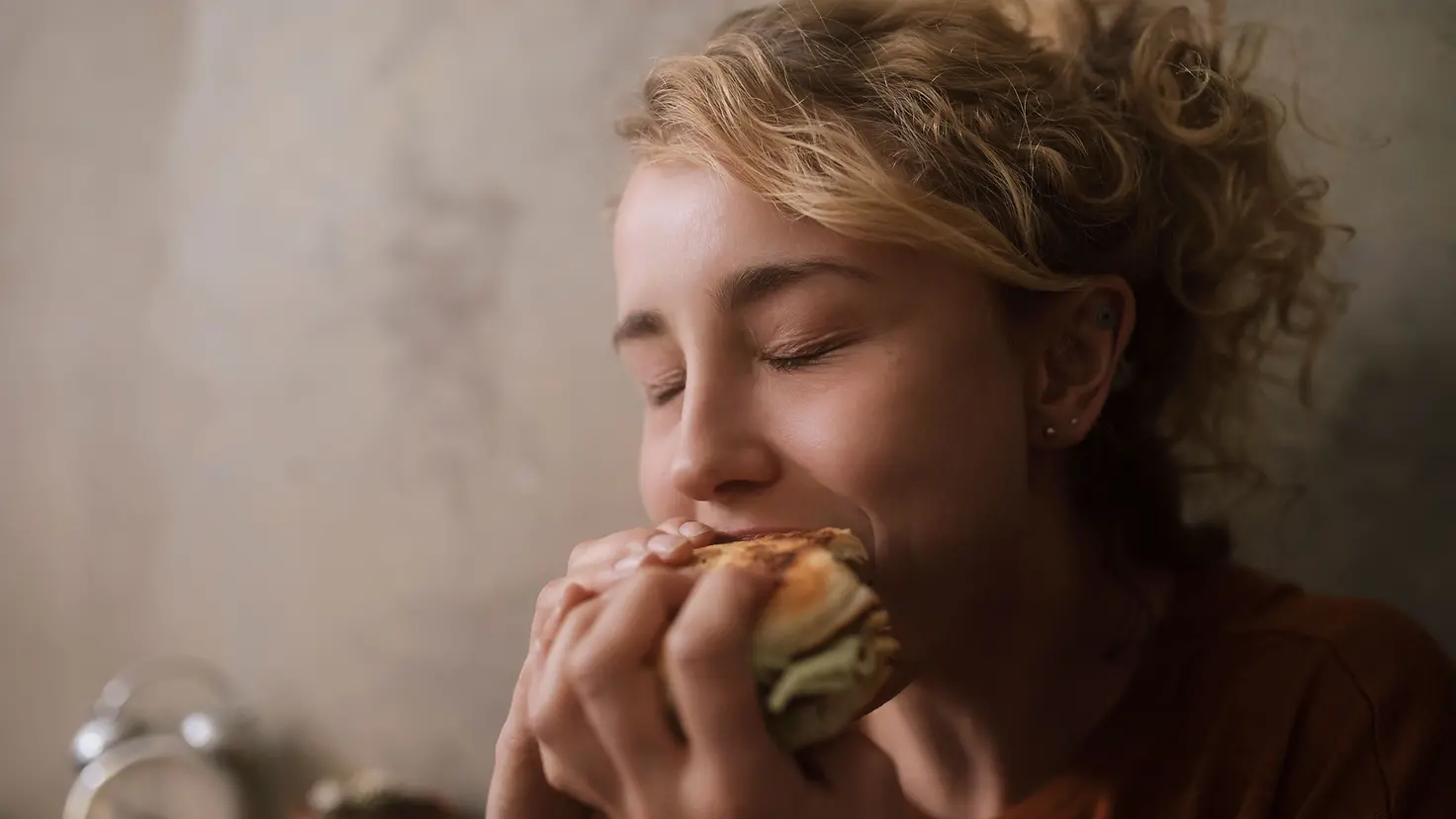 Eine junge Frau isst genussvoll einen Hamburger mit geschlossenen Augen