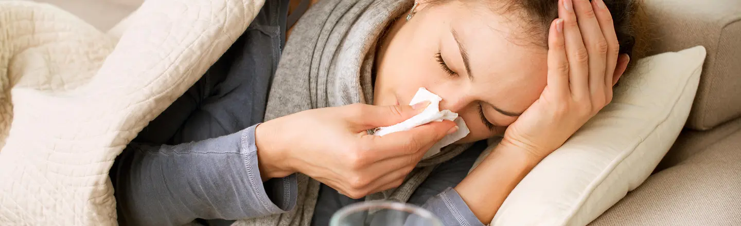 Eine Frau mit Grippe liegt auf dem Sofa und schnäuzt ihre Nase.