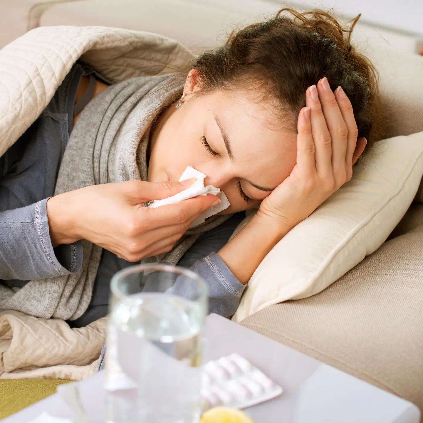 Eine Frau mit Grippe liegt auf dem Sofa und schnäuzt ihre Nase.