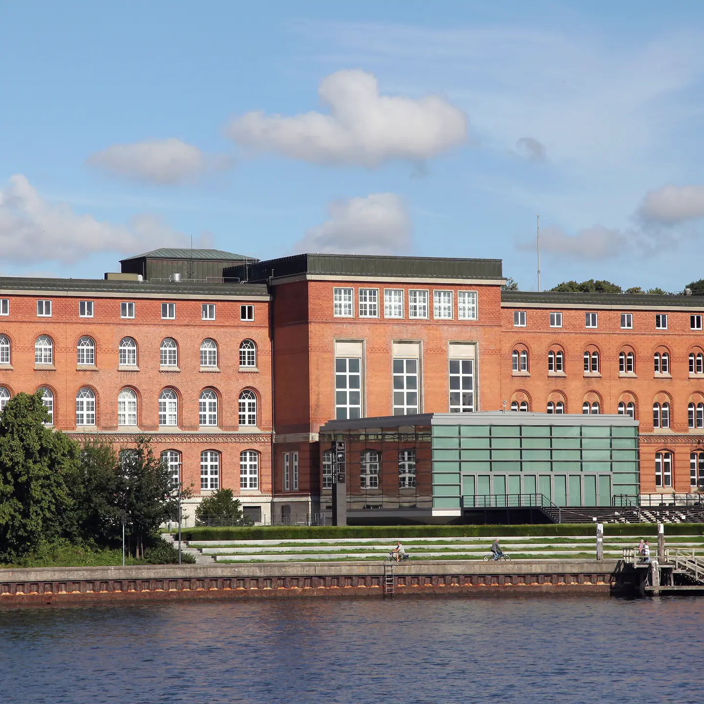 ein roter Klinkerbau auf drei Etagen mit Rundbogenfenstern und gläsernem Vorbau an der Kieler Förde