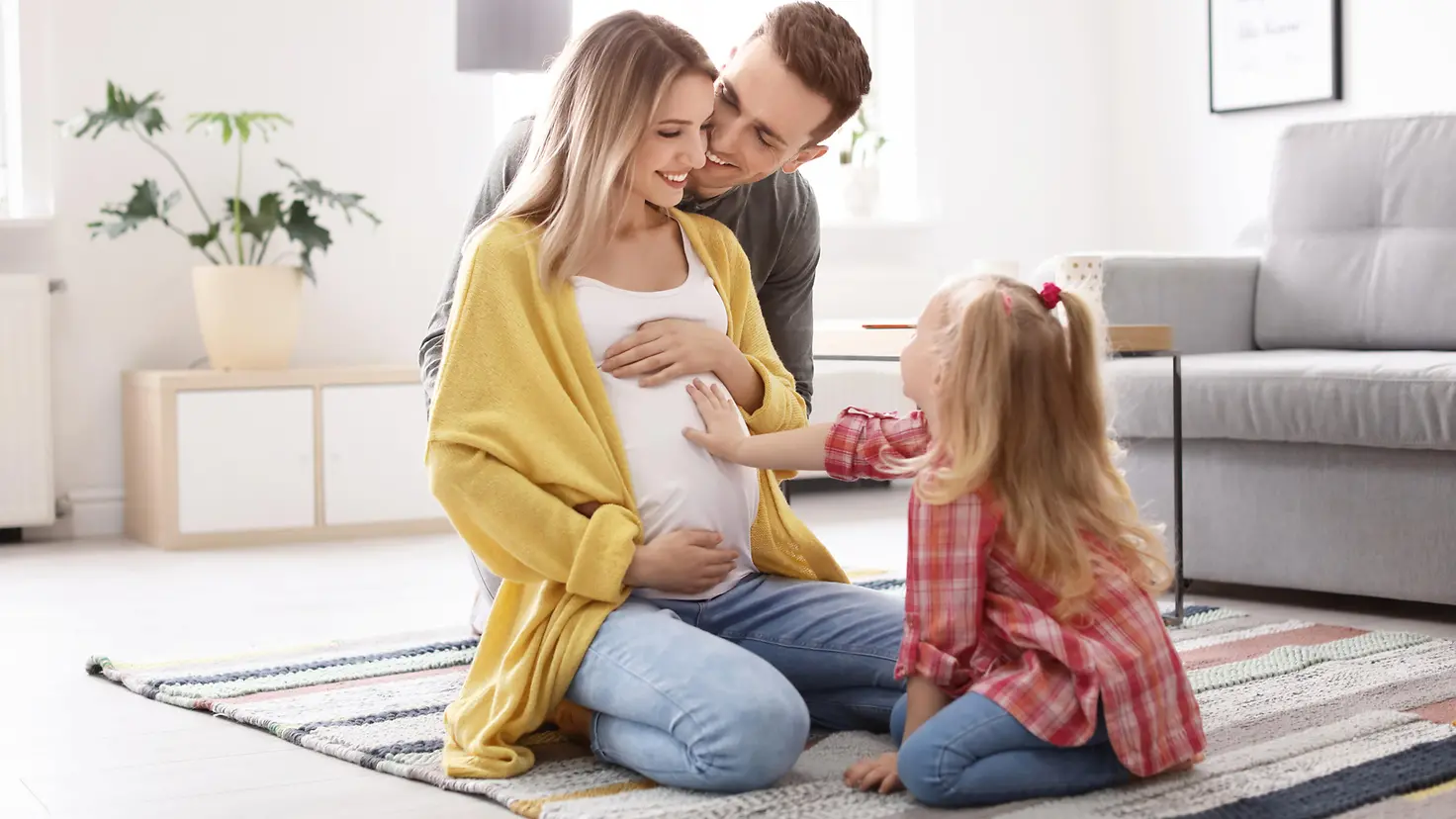 Eine schwangere Frau, ihr Mann und ein Mädchen legen die Hände auf den Bauch der Mutter.