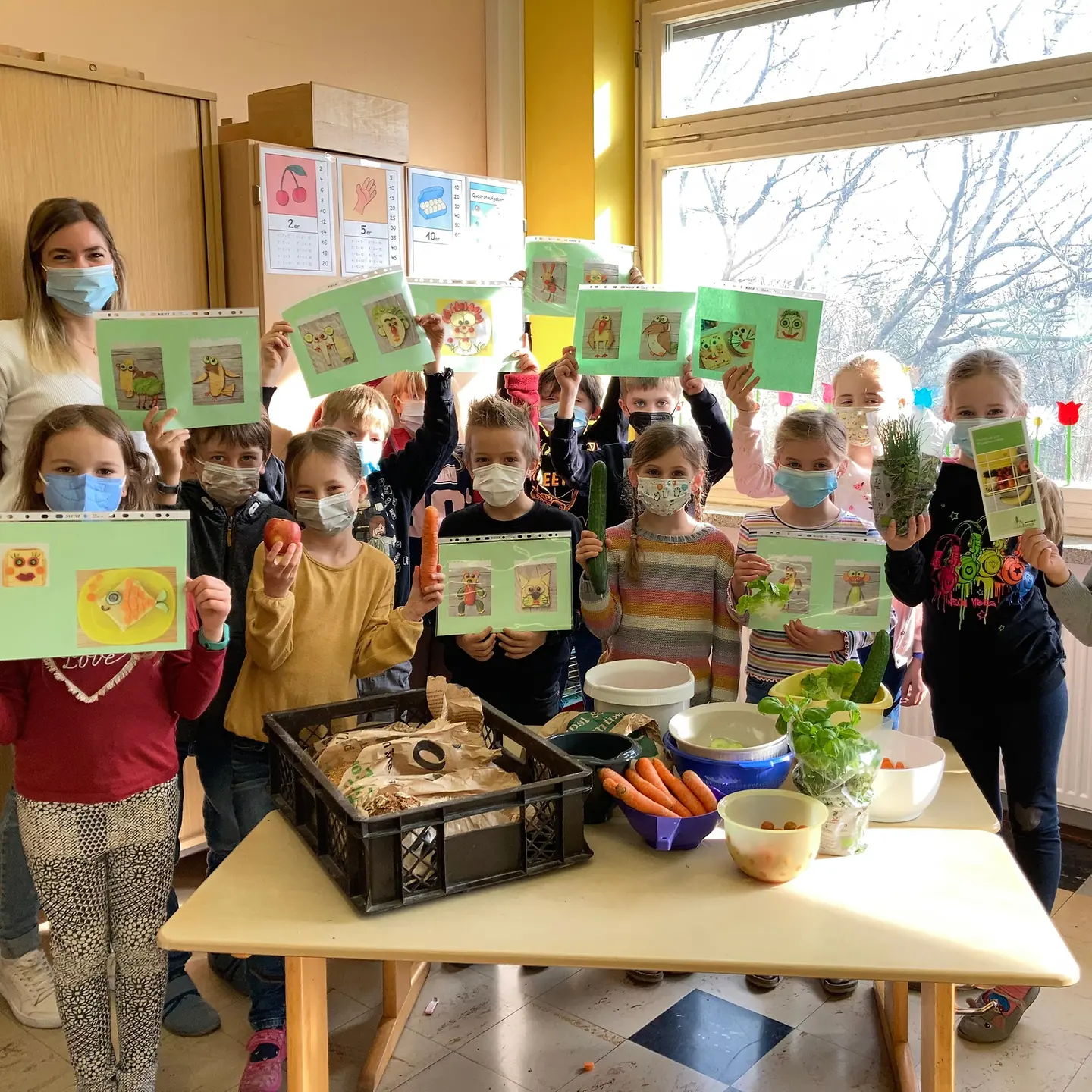 Gruppenfoto von einer jungen Frau und Grundschulkindern, die zusammen ein gesundes Frühstück zubereitet haben.