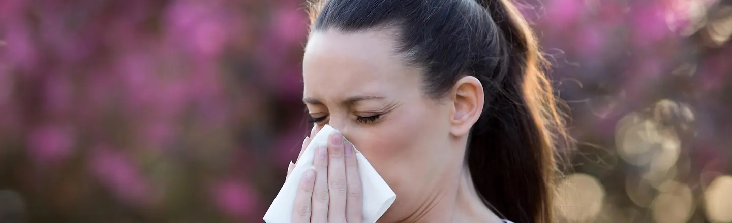 Das Bild zeigt eine Frau, die sich ihre Nase putzt.