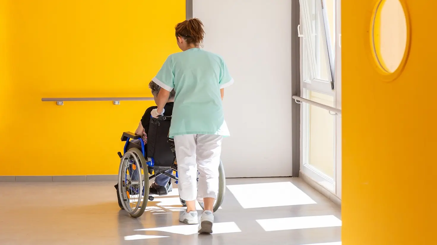 Eine Pflegerin schiebt eine ältere Dame im Rollstuhl
