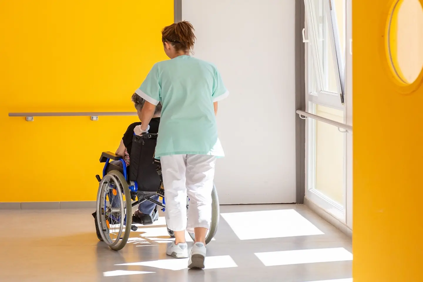 Eine Pflegerin schiebt eine ältere Dame im Rollstuhl