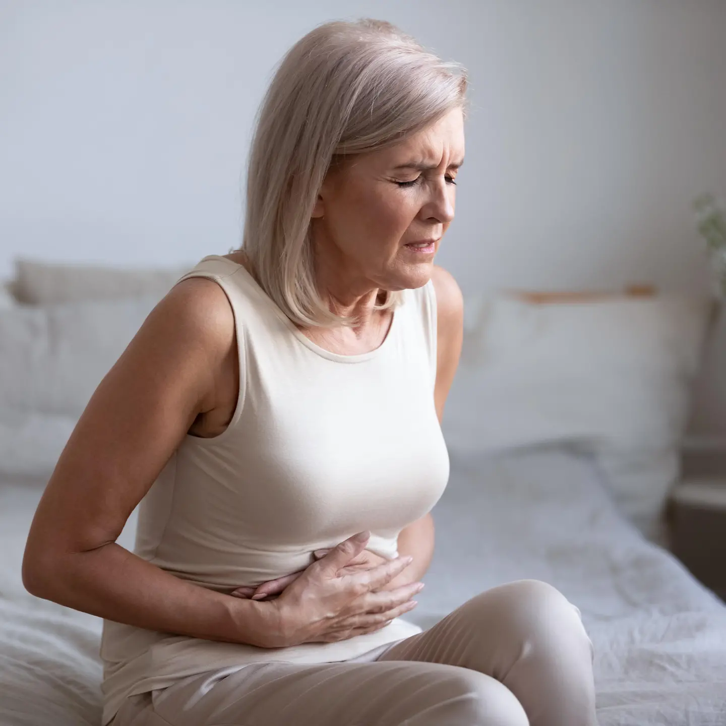 Eine Frau mit schmerzverzehrten Gesicht fasst sich an ihren Bauch.