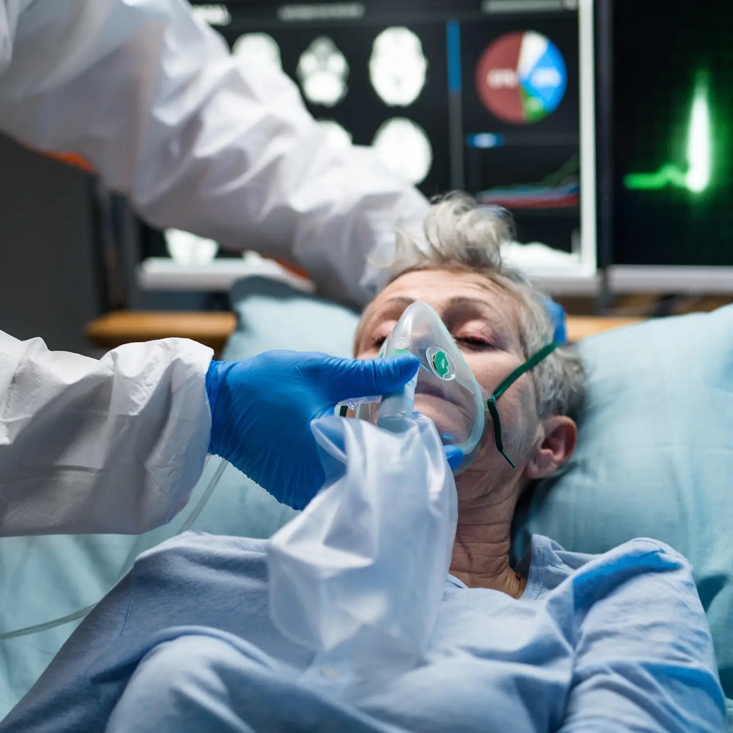 Eine ältere Person liegt im Krankenhaus und wird von einer Person im Schutzanzug ärztlich behandelt.