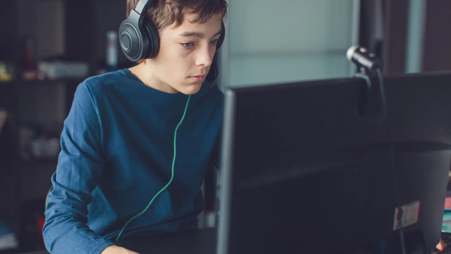 Ein Junge sitzt mit Headset vor einem Computer und spielt ein Computerspiel.