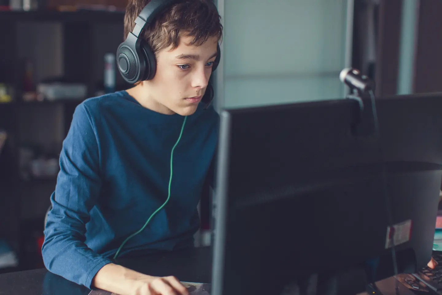 Ein Junge sitzt mit Headset vor einem Computer und spielt ein Computerspiel.