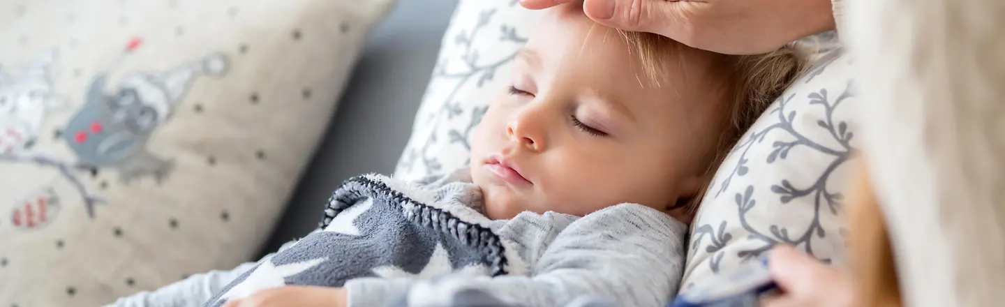 Ein Kind schläft. Die Mutter hält die Hand an die Stirn und misst Fieber.
