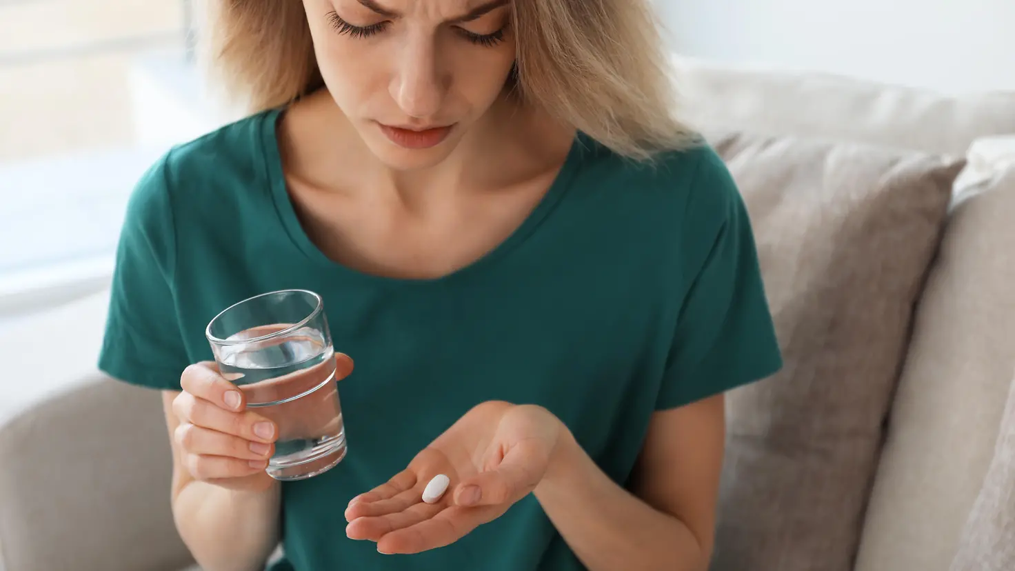 Eine Frau hält eine Tablette in einer Hand und ein Glas Wasser in der anderen.