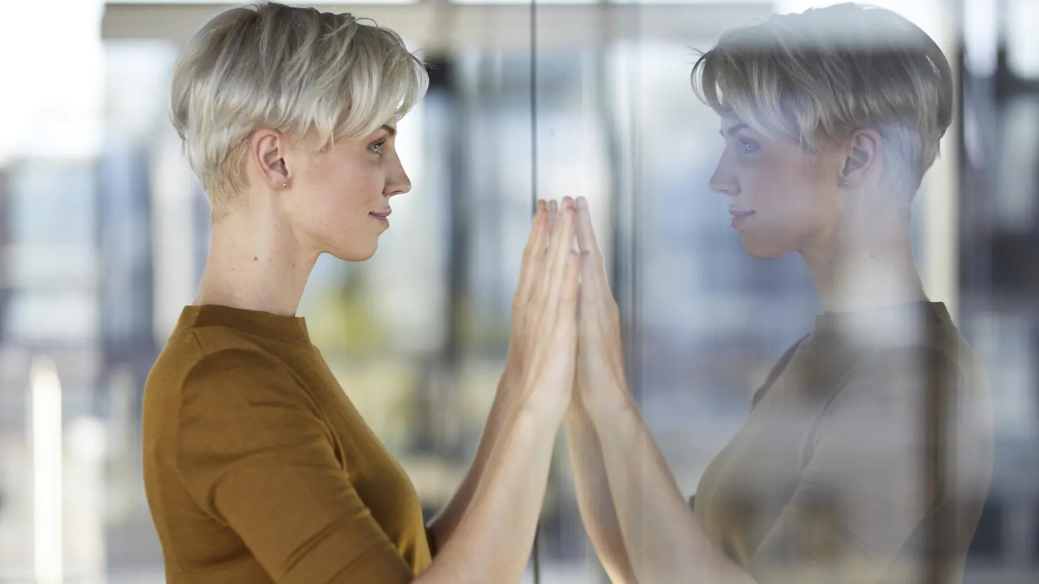 Eine junge Frau blickt in eine Scheibe in ihr Spiegelbild