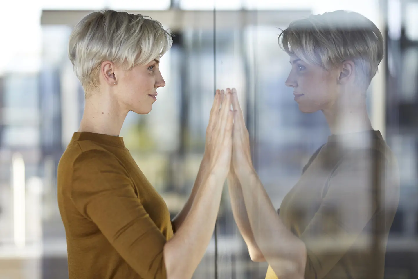 Eine junge Frau blickt in eine Scheibe in ihr Spiegelbild
