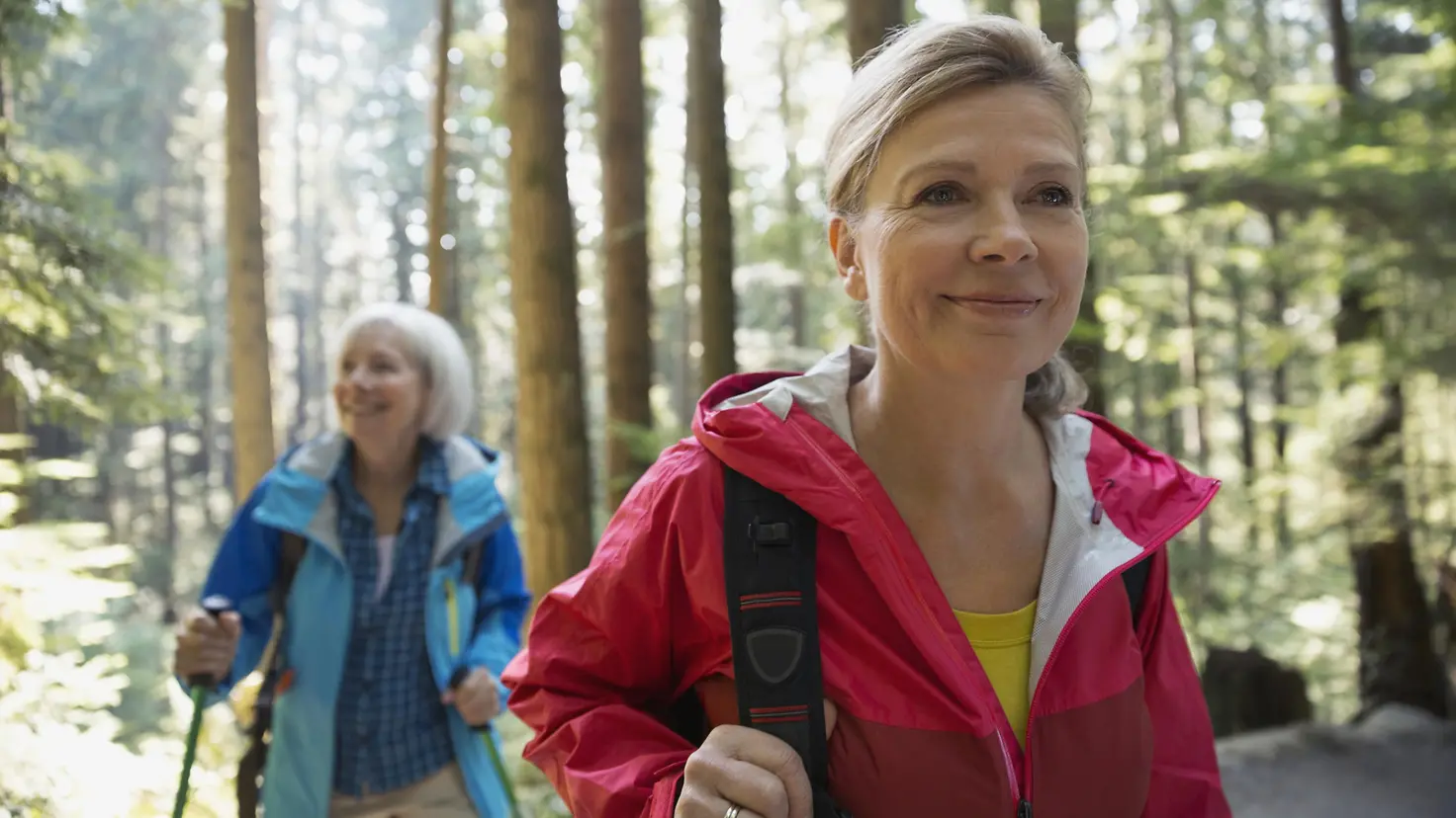 Zwei Frauen mittleren Alters wandern zusammen durch den Wald und sehen glücklich aus.