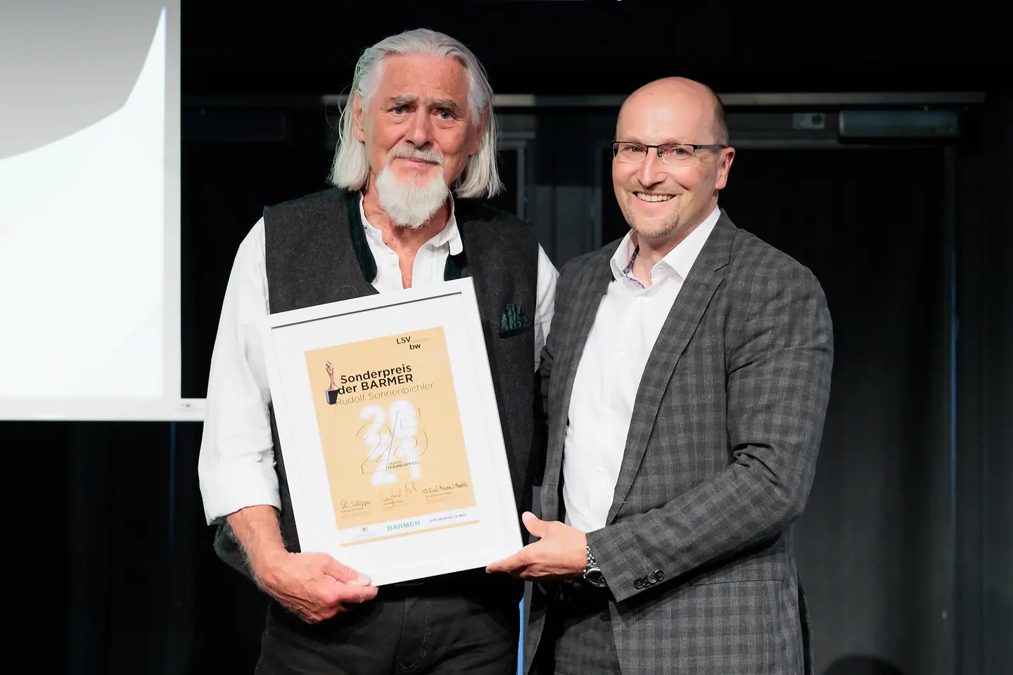 zwei Männer halten lächelnd die Urkunde "Sonderpreis der BARMER" in die Kamera