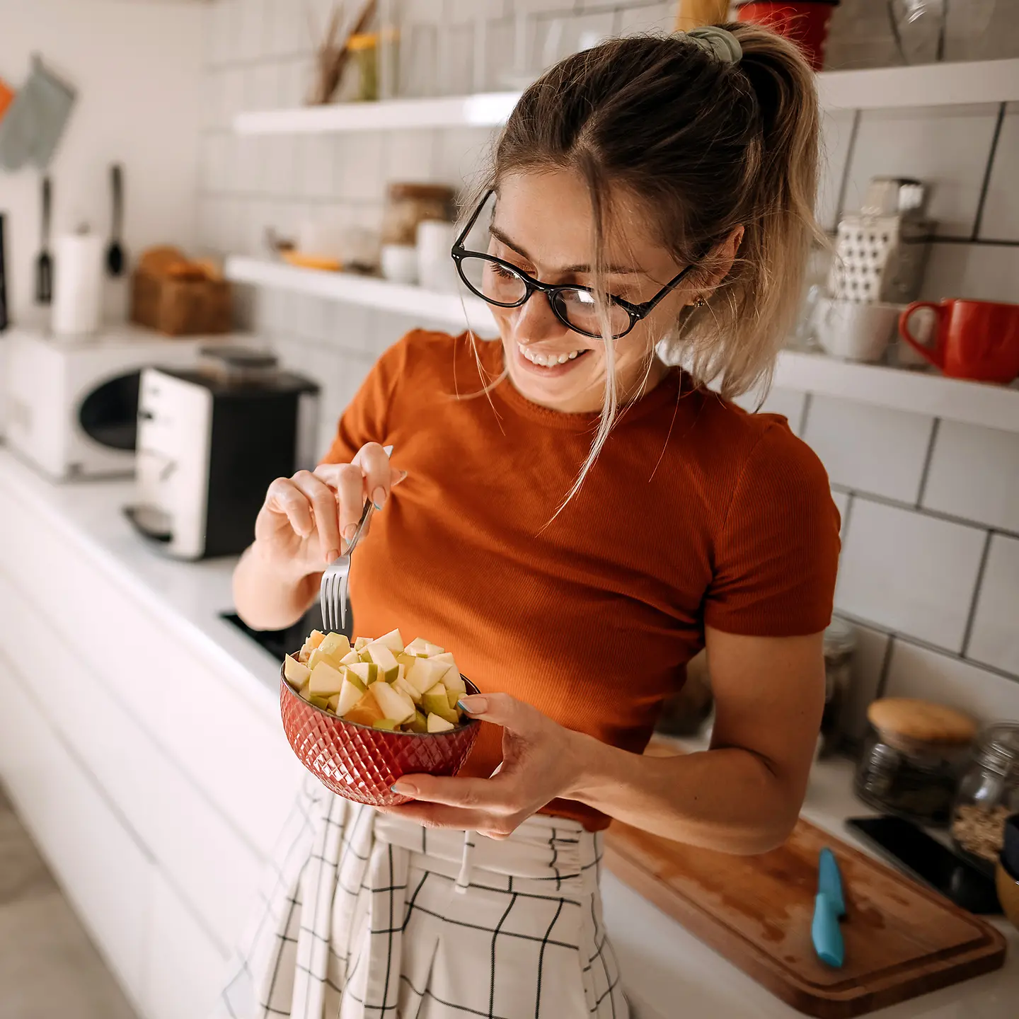 Eine junge Frau steht in ihrer Küche und hält einen Obstsalat in der Hand