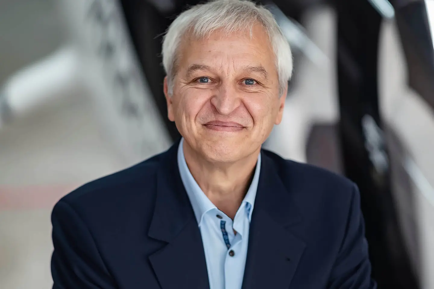 Ein älterer Herr hat die Arme vor der Brust verschränkt und lächelt in die Kamera