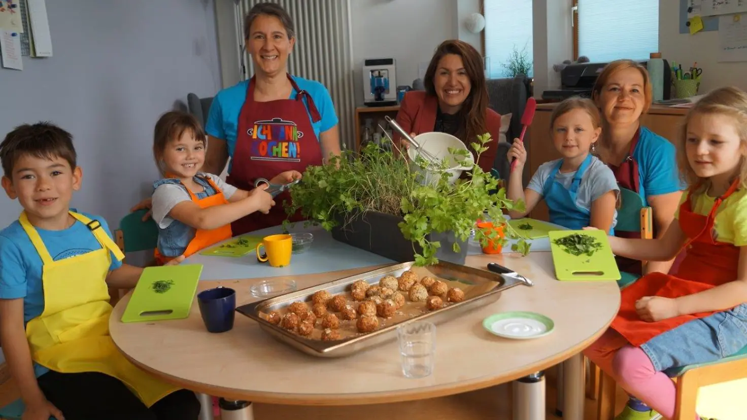 Kita-Kinder sitzen an einem Tisch und bereiten Essen zu mit Kita-Personal und BARMER-Vertreterin.