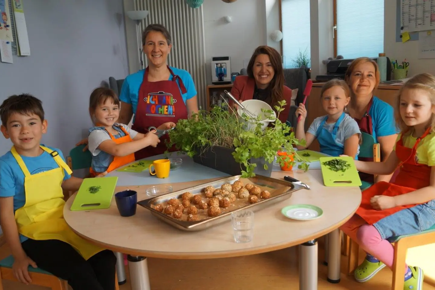 Kita-Kinder sitzen an einem Tisch und bereiten Essen zu mit Kita-Personal und BARMER-Vertreterin.