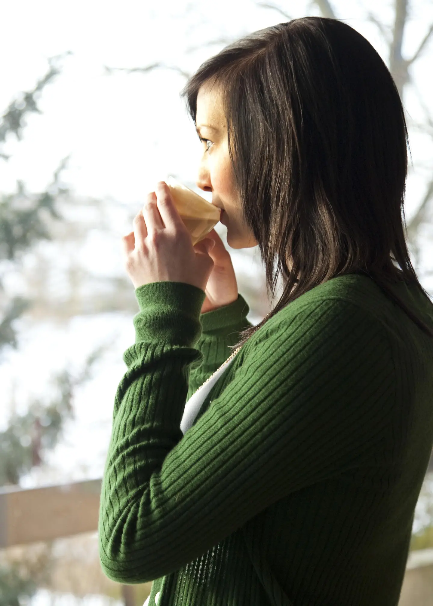 Junge Frau trinkt ein heißes Getränk und schaut aus dem Fenster