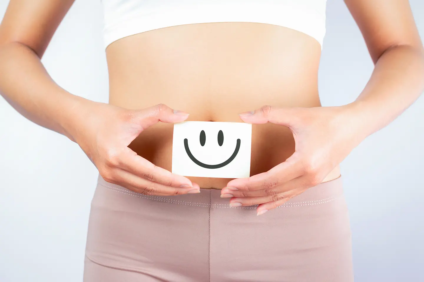 Eine Frau hält einen Zettel vor ihren Bauch. Auf dem Zettel ist ein positiver Smiley abgebildet.