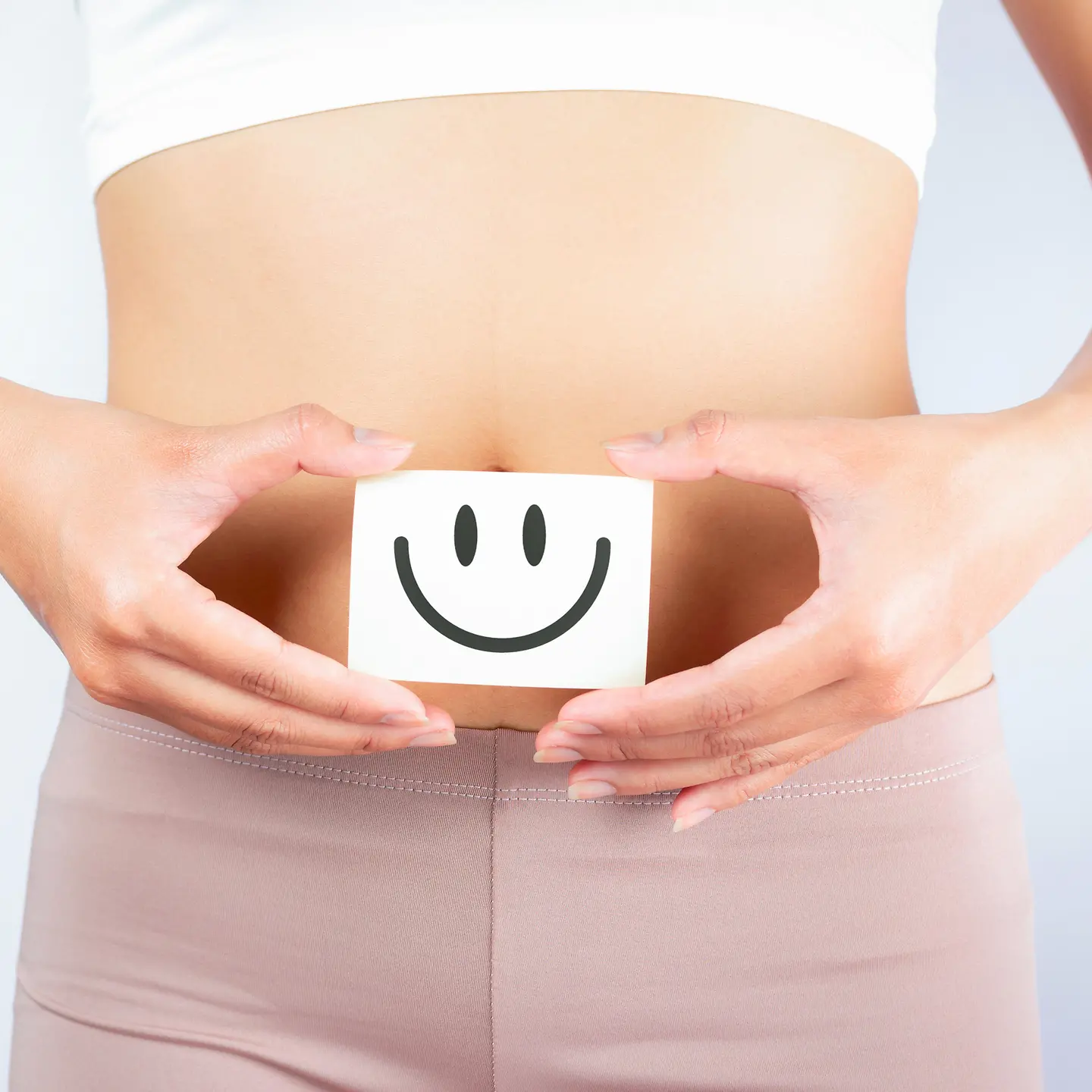 Eine Frau hält einen Zettel vor ihren Bauch. Auf dem Zettel ist ein positiver Smiley abgebildet.