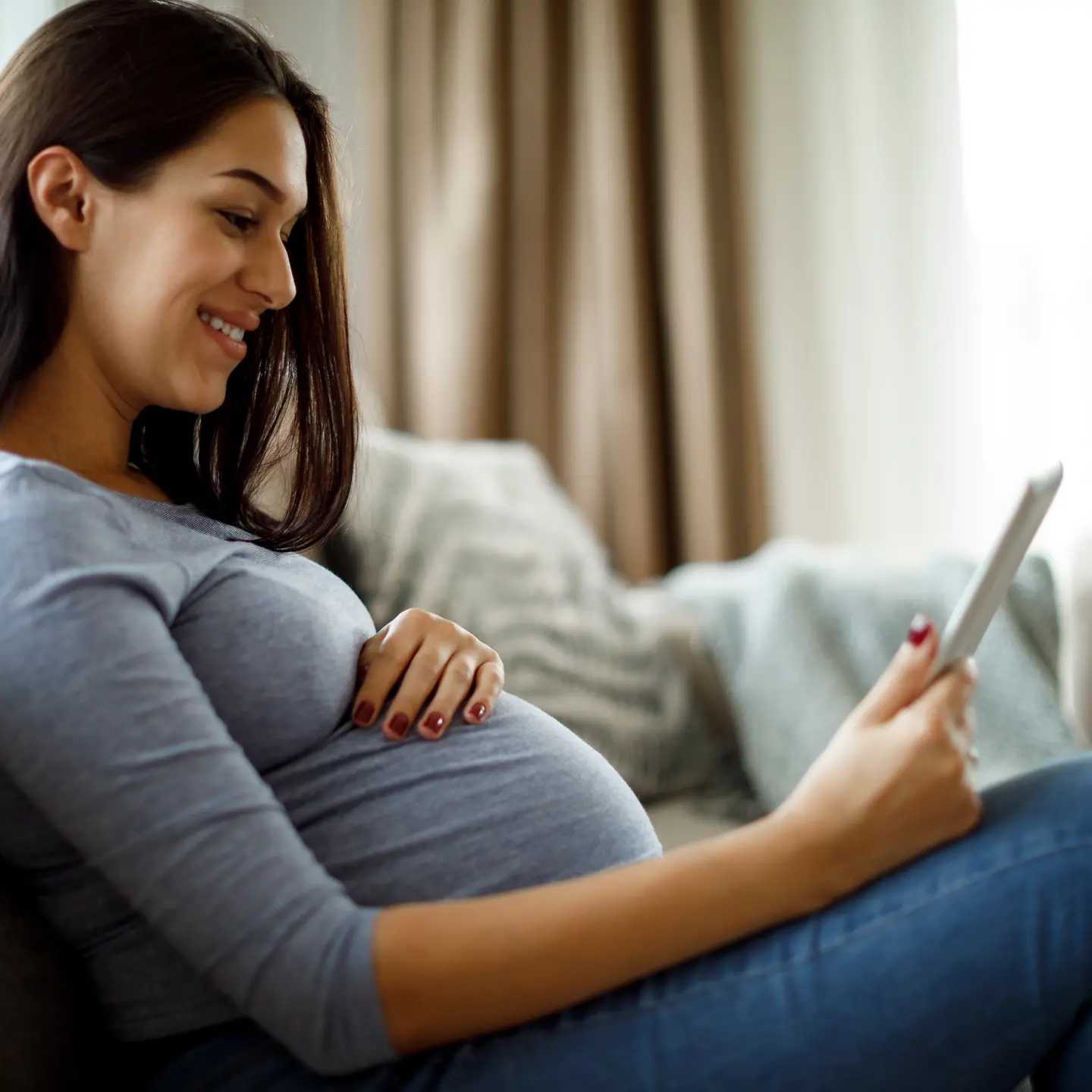 Eine schwangere Frau sitzt mit dem iPad auf dem Sofa