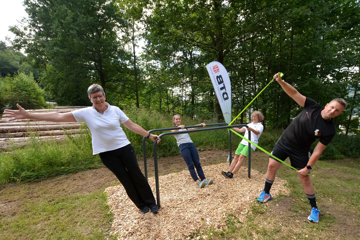 Vier Menschen machen Übungen an einem Barren des Fitness-Trails.
