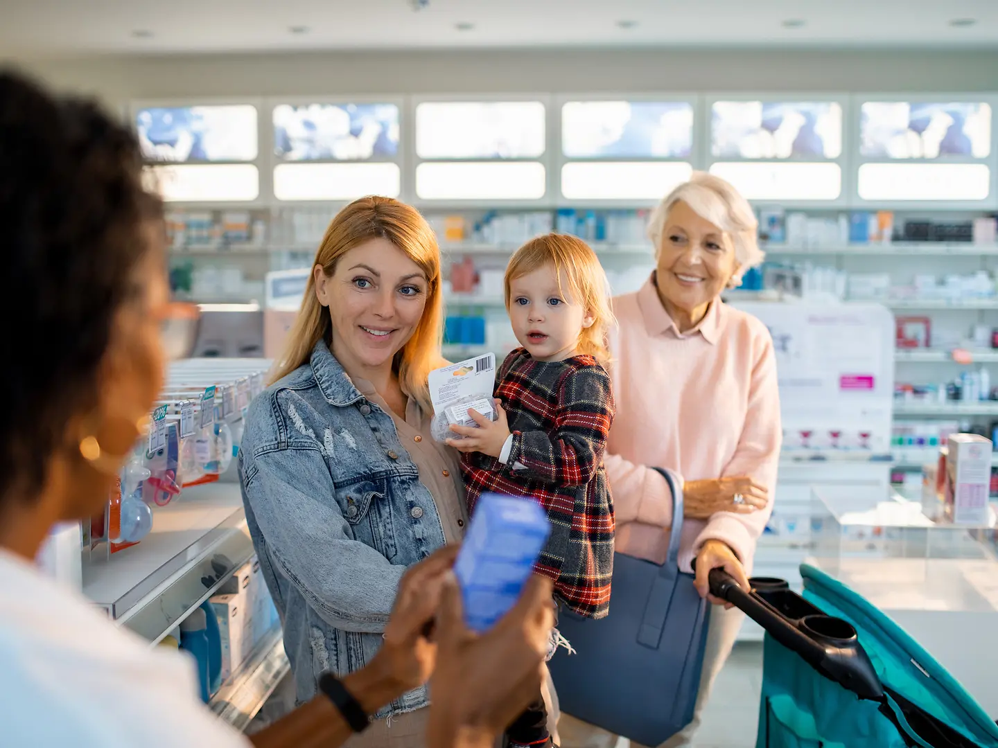 Eine Mutter mit Kind und Oma kaufen in der Apotheke ein Medikament