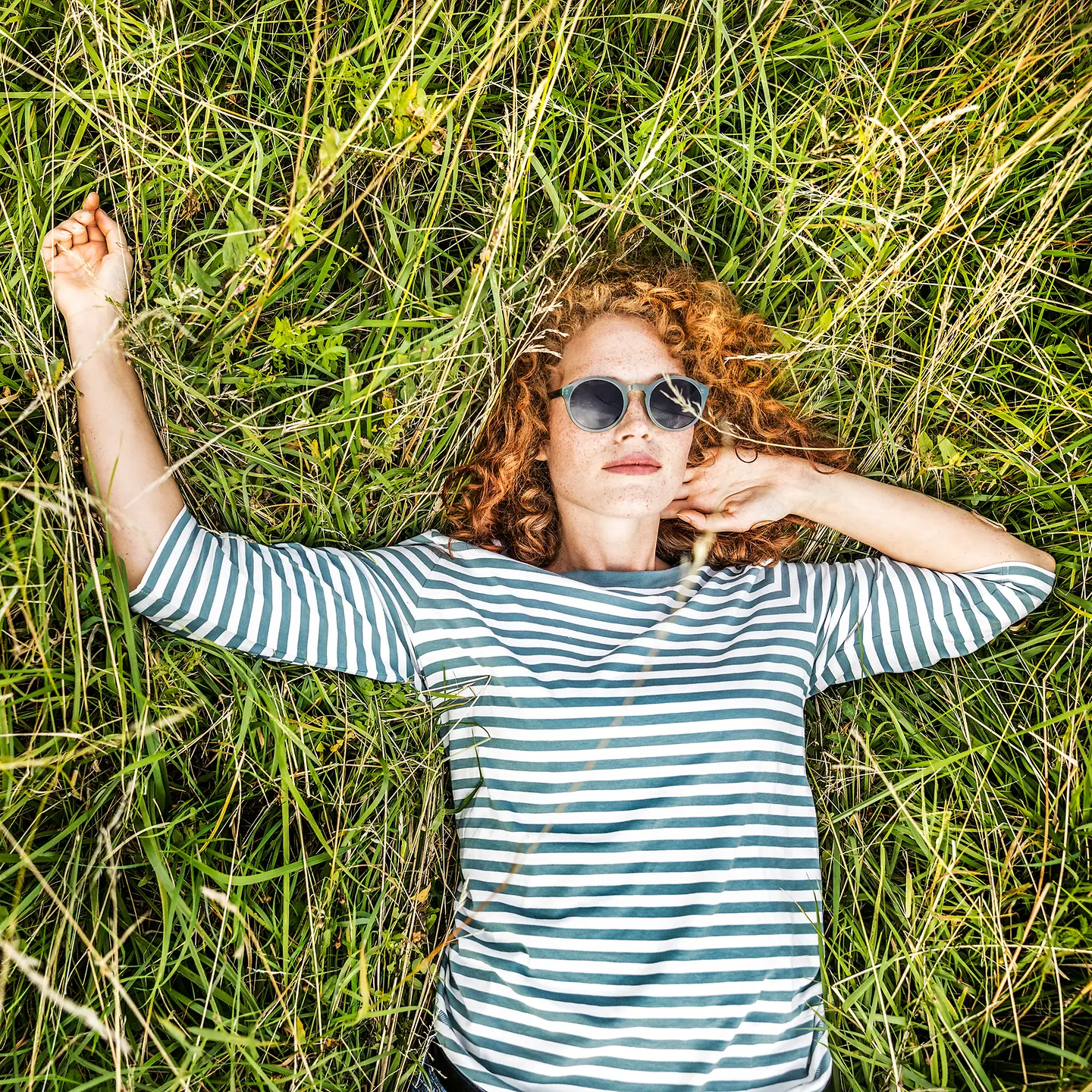 Eine junge Frau mit Sonnenbrille liegt auf einer Wiese und schützt ihre Haut